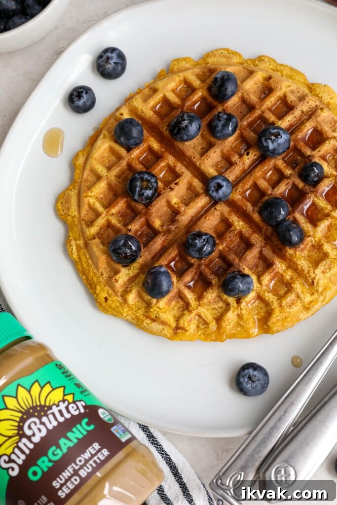 Sweet Potato Waffles served on a plate topped with maple syrup and blueberries with SunButter jar