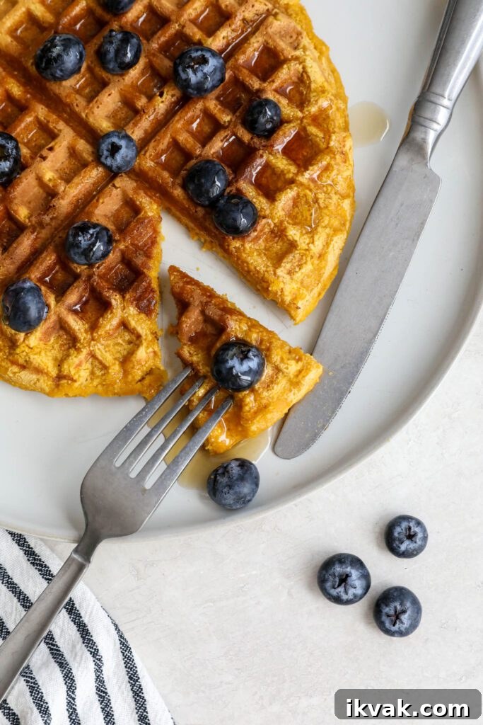 Sweet Potato Waffles served on a plate topped with maple syrup and blueberries with a triangle cut out with fork and knife
