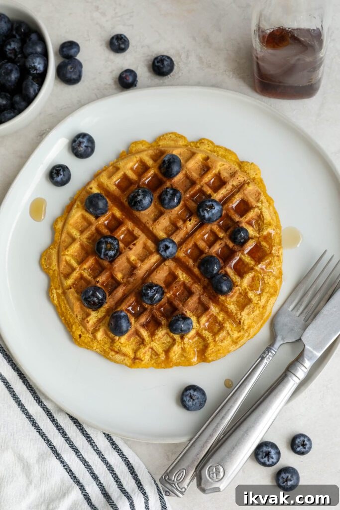 Sweet Potato Waffles served on a plate topped with maple syrup and blueberries with a fork and knife