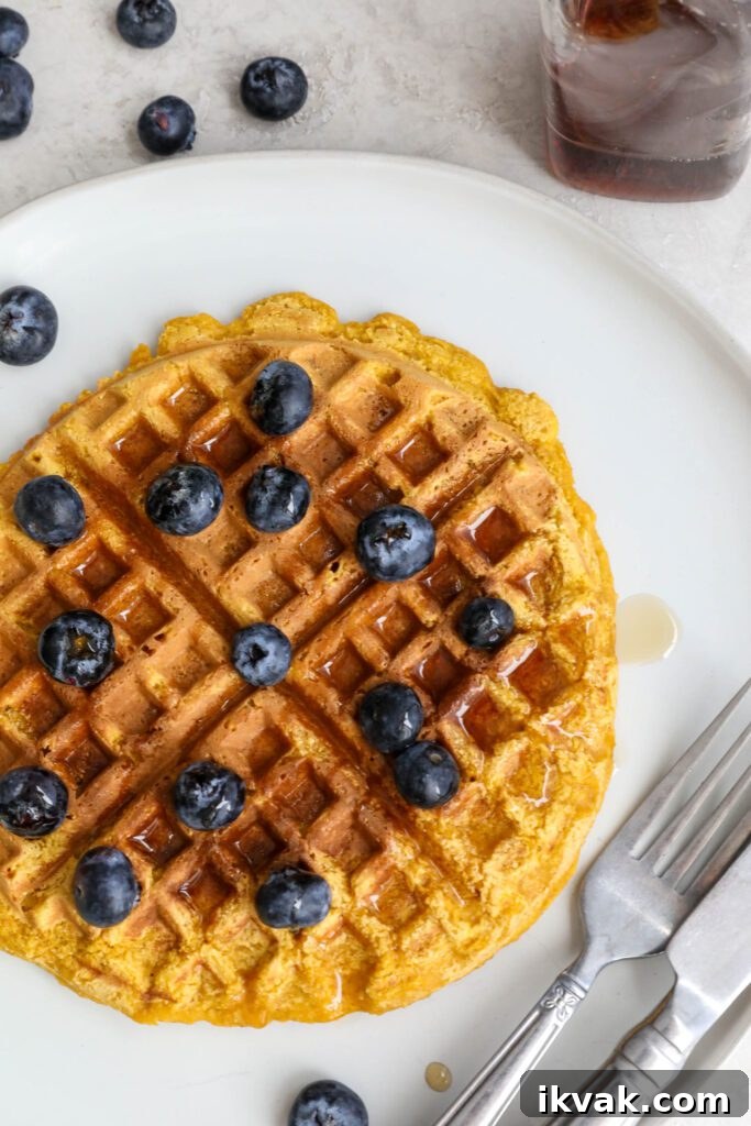 Sweet Potato Waffles served on a plate topped with maple syrup and blueberries with fork and knife