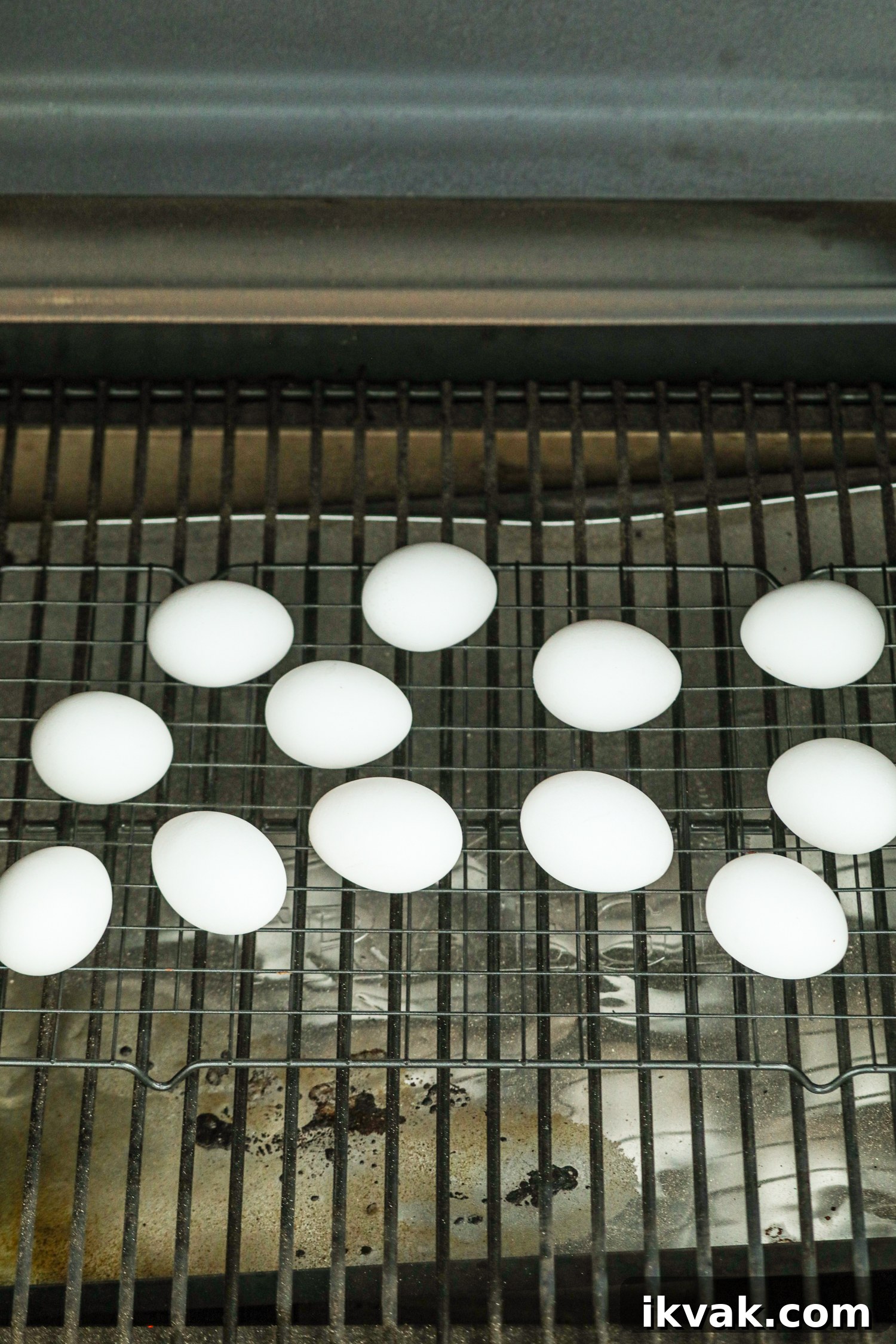 The image shows several white eggs placed on a wire rack inside a smoker or grill.
