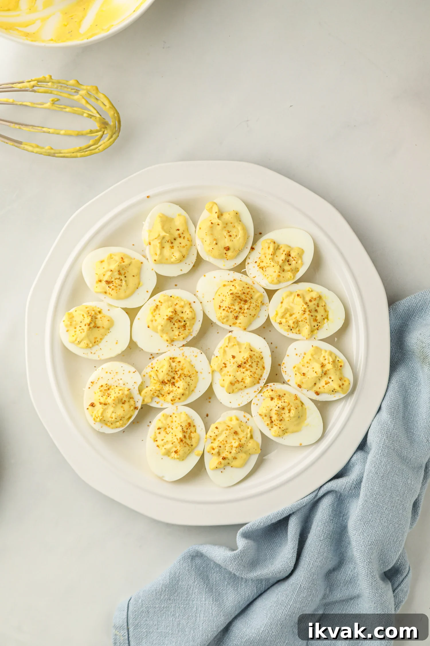 A white plate with smoked deviled eggs, each filled with a creamy yellow yolk mixture and sprinkled with seasoning.
