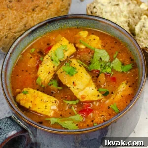 spicy fish soup in a blue bowl with fresh coriander sprinkled over the top and crusty bread on the side