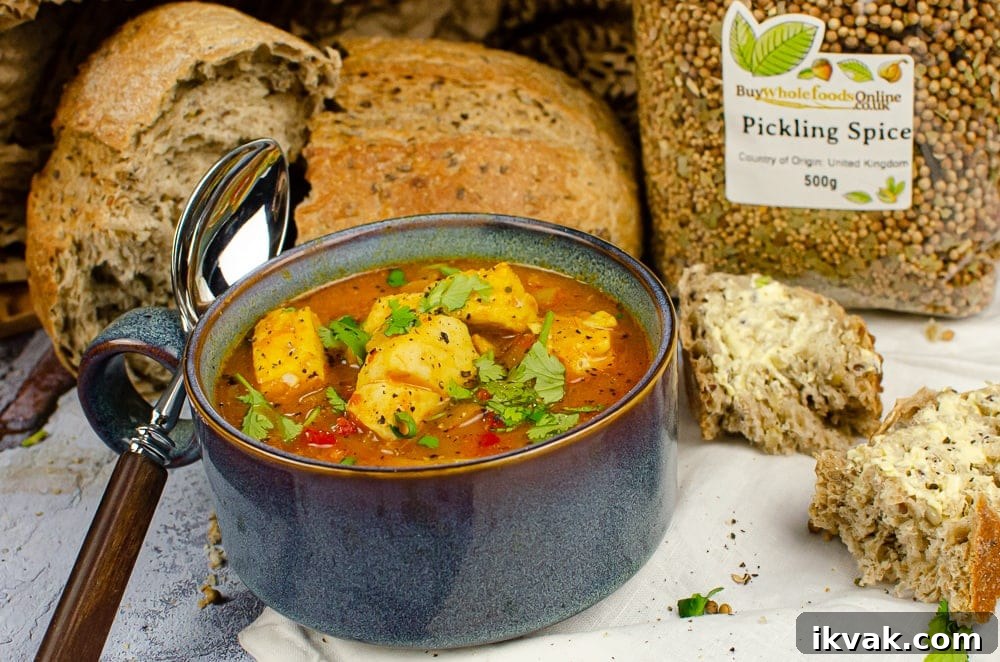 Spicy fish soup in a blue bowl with chopped coriander on top with crusty bread and a bag of pickling spice on the side