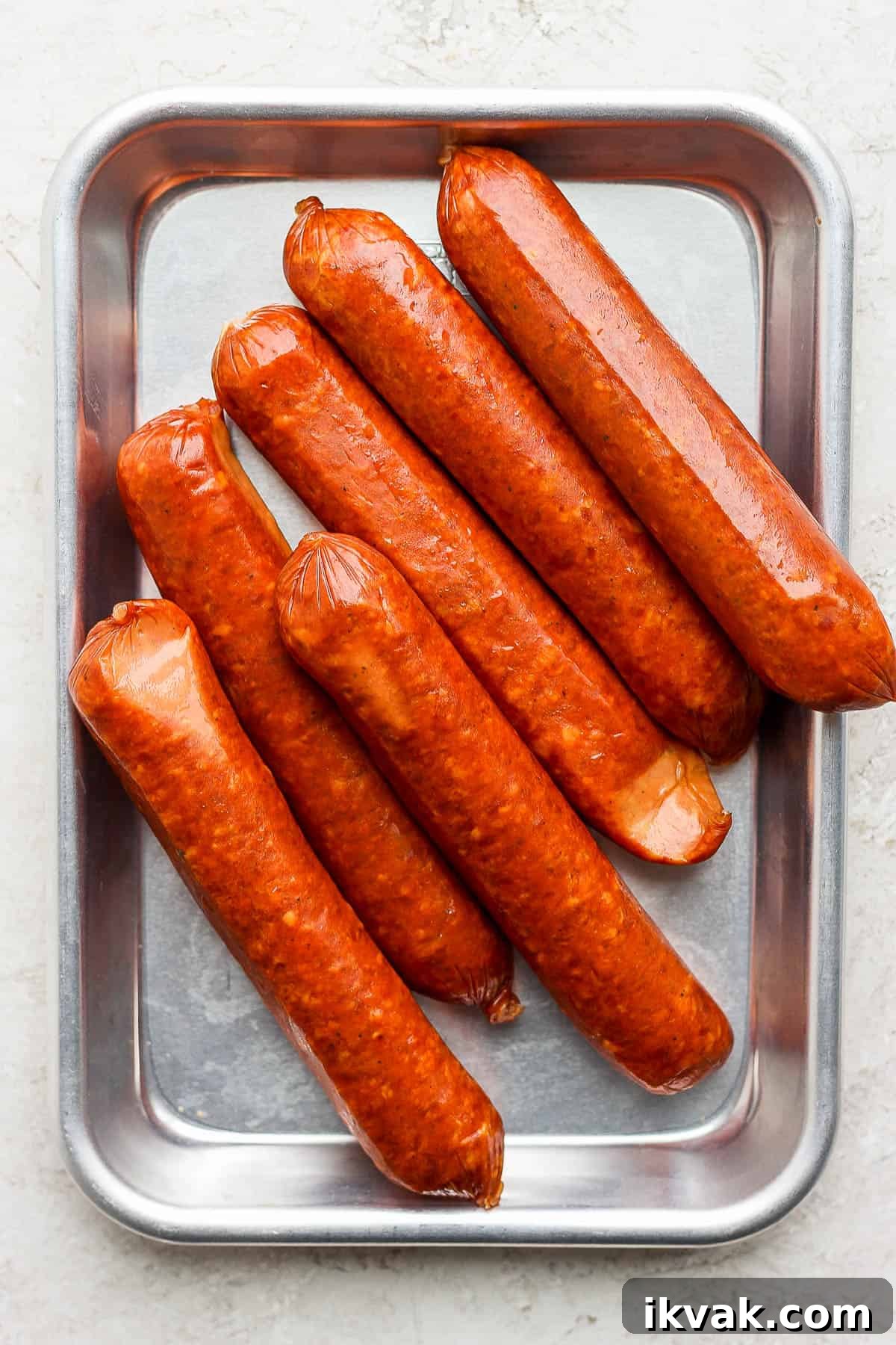 Precooked brats on a metal tray before grilling.