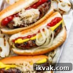 Top down shot of a small pan of 3 grilled brats in buns with onion, ketchup and mustard.