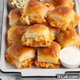 Tangy BBQ Chicken Sliders Recipe for Crowd-Pleasing Sandwiches 5 A tray of baked Buffalo Chicken Sliders filled with shredded buffalo chicken and melted cheese, topped with golden brown buns. A small dish of ranch dressing and a bowl of blue cheese crumbles are served on the side. Try this Buffalo Chicken Sliders Recipe!.
