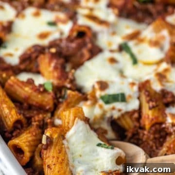 close-up of wooden spoon dipped in white baking dish of rigatoni al forno