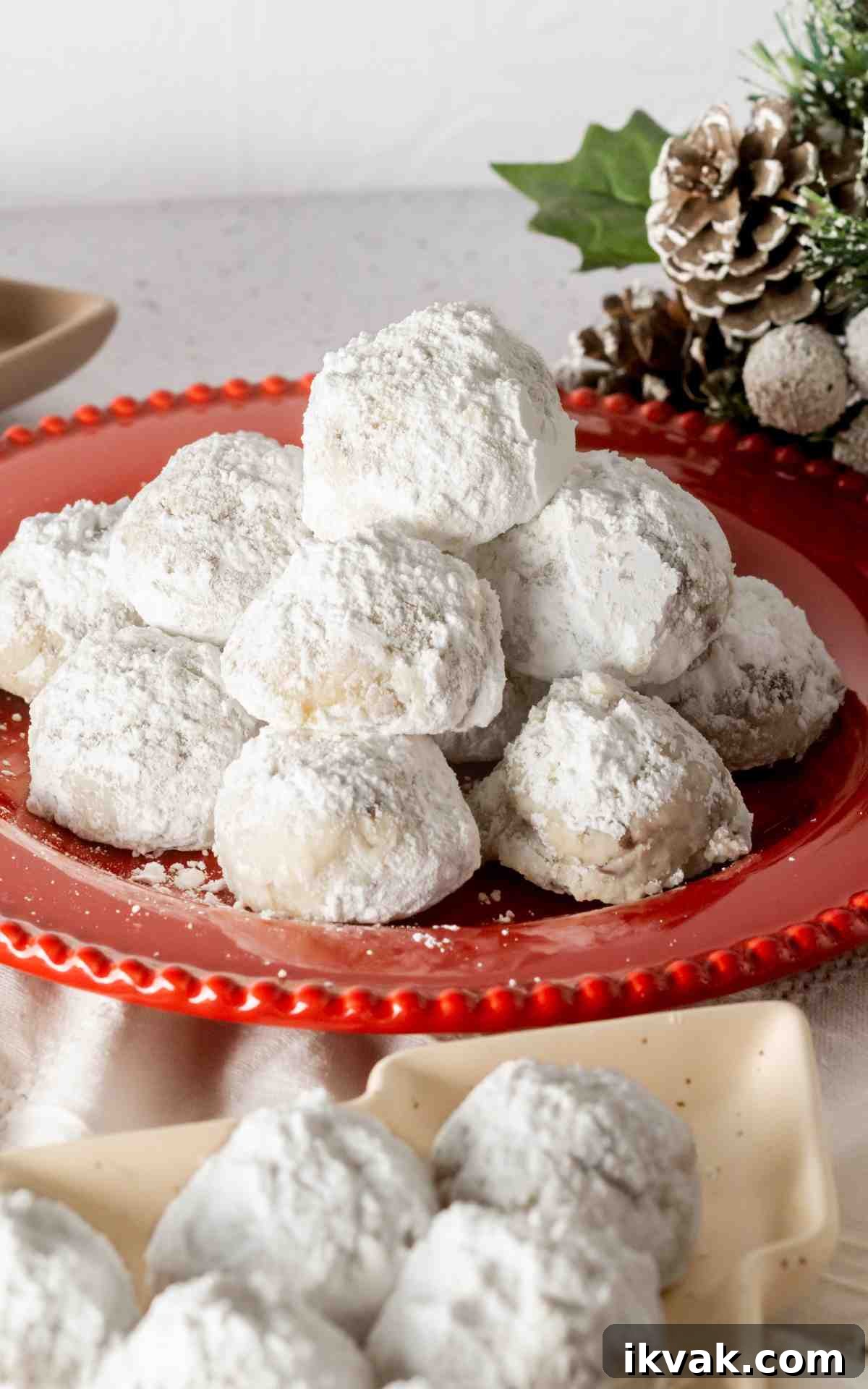 Snowball cookies on a red plate with another plate in front of it.