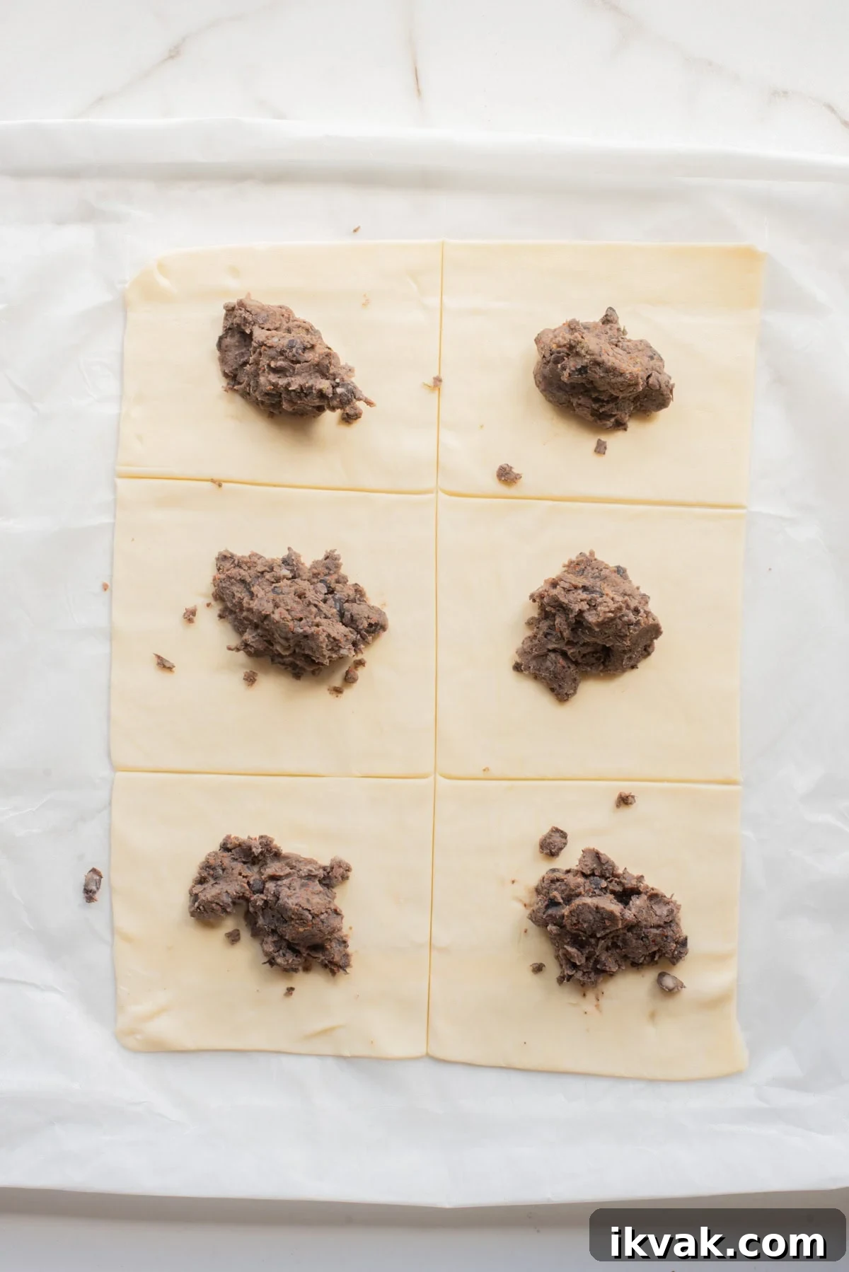 Puff pastry sheets cut into rectangles with spoonfuls of bean mixture placed on top.