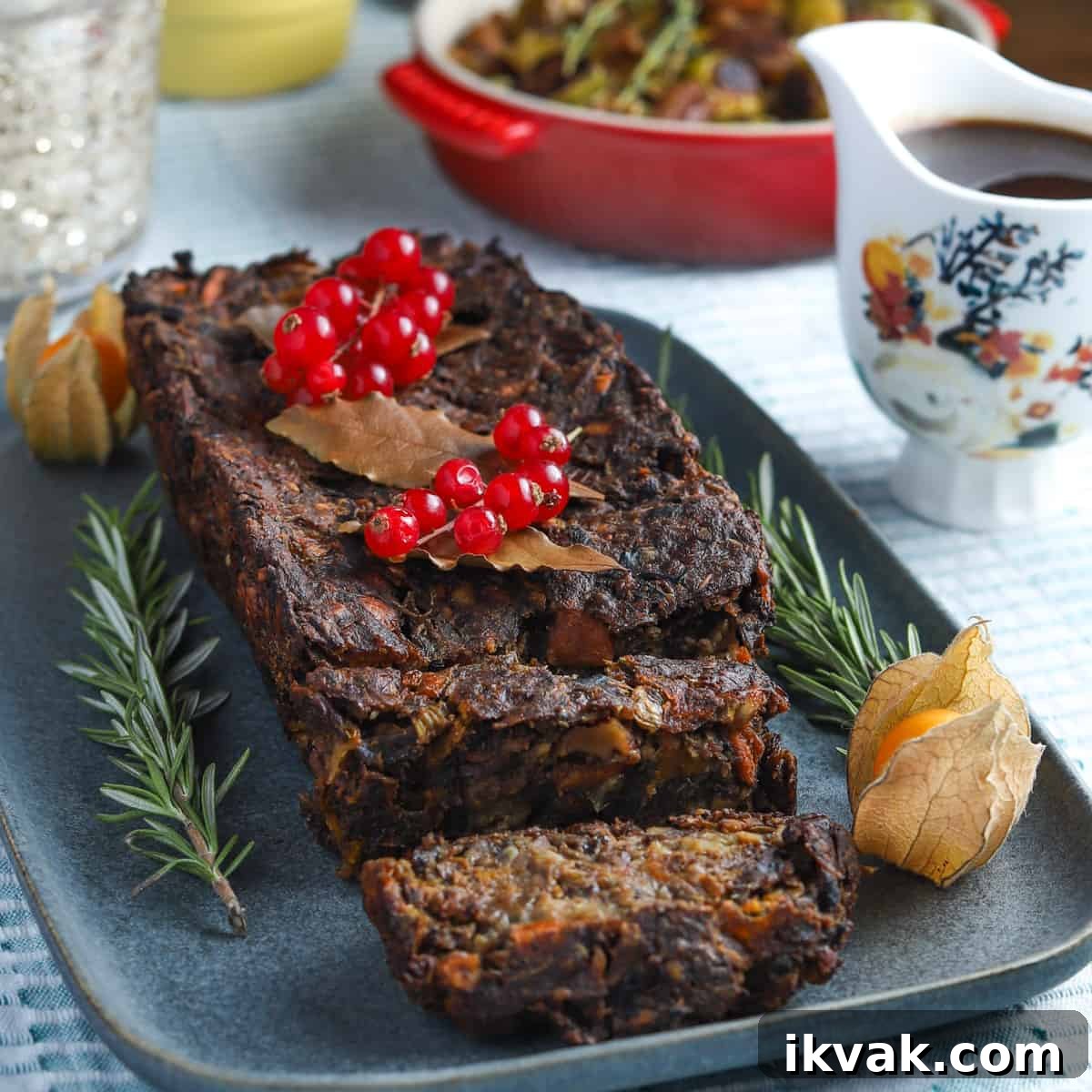 Photo of vegan & gluten-free nut roast on a blue-grey plate garnished with red currants, rosemary and cape gooseberries.