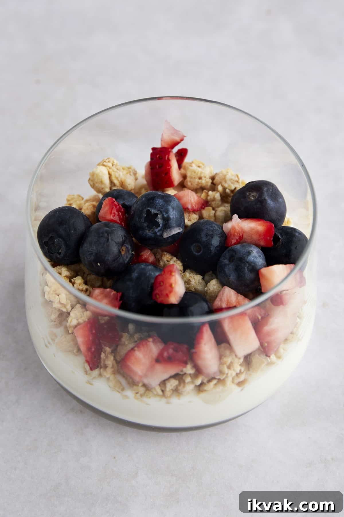 A glass jar with yogurt, granola, chopped strawberries, and blueberries. 
