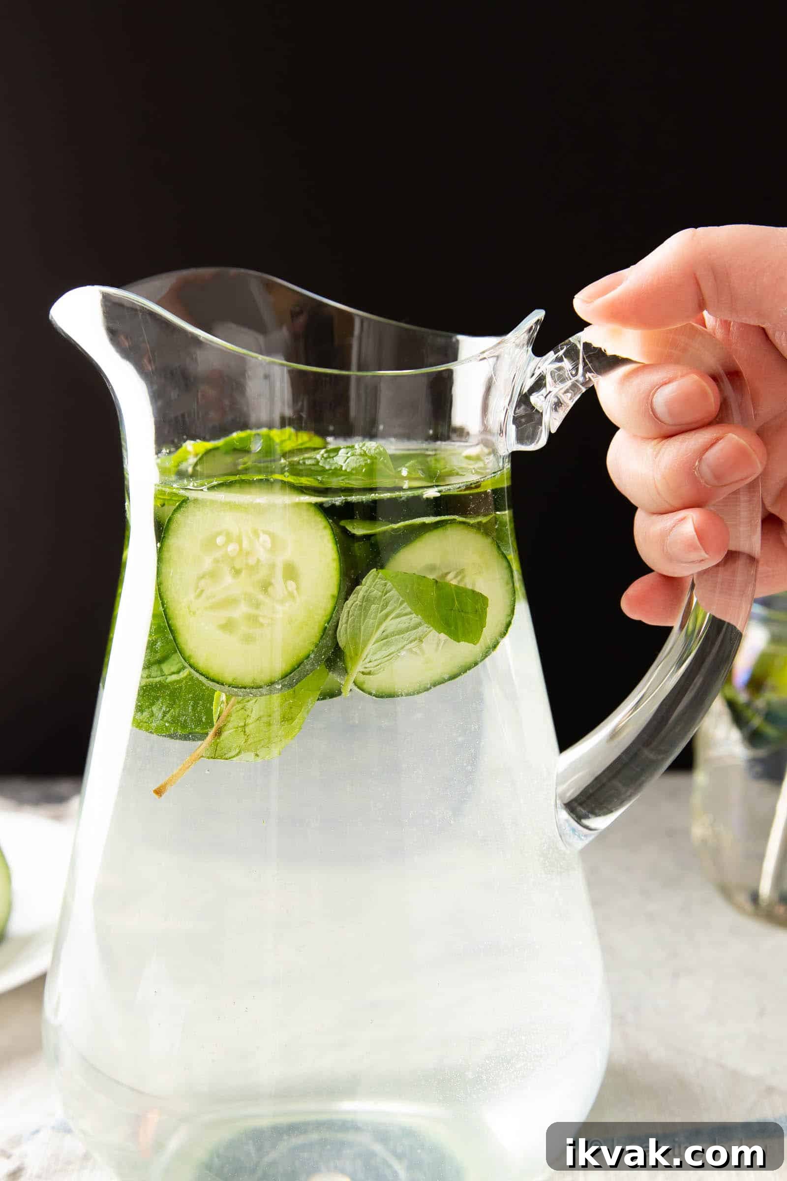 Hand holding a pitcher of cucumber and mint water