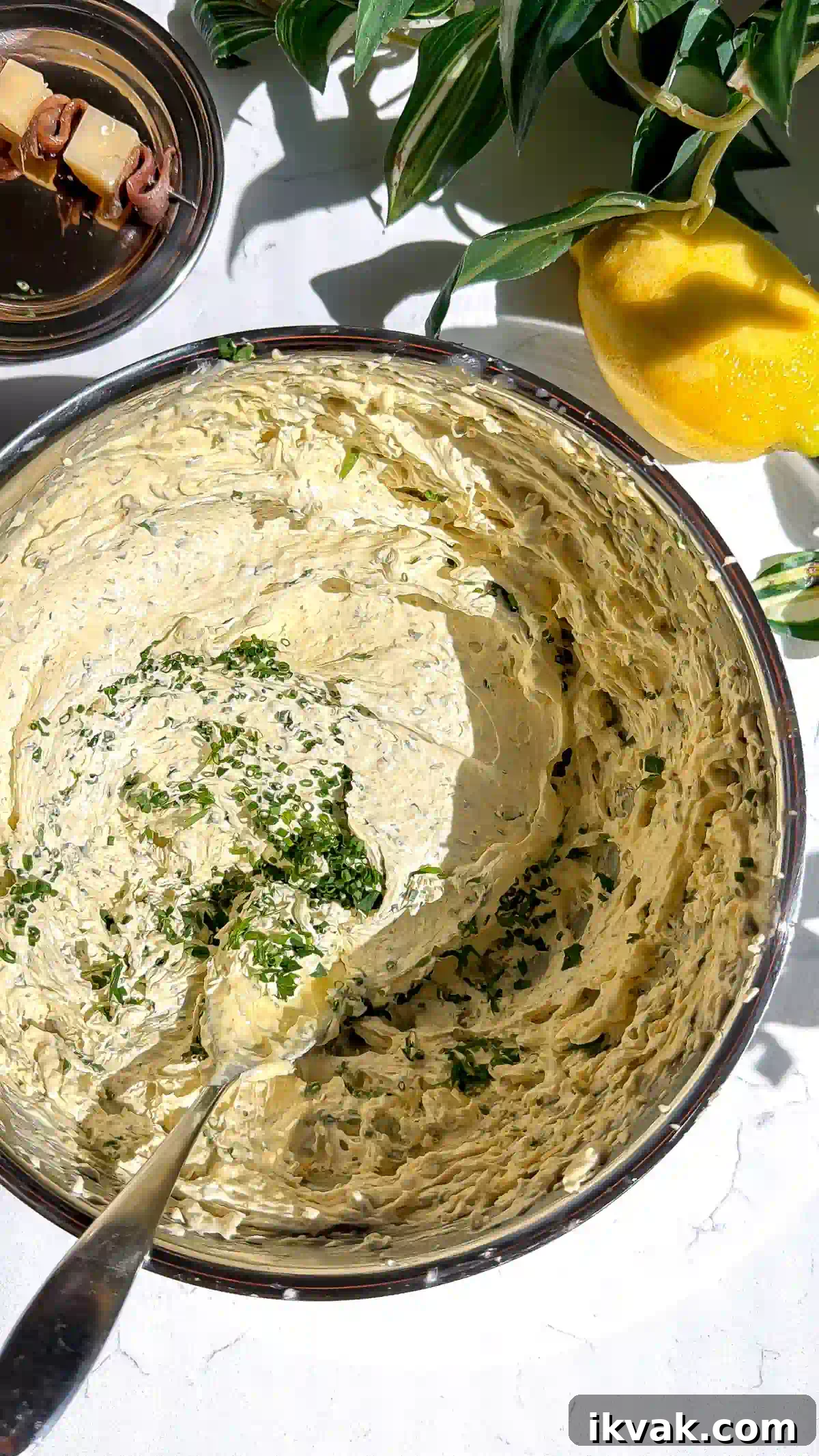 Caesar-Style Whipped Butter: Creamy Dressing-Inspired Spread 3 A top-down view of fluffy Caesar whipped brown butter in a metal mixing bowl with a spoon resting inside, sprinkled with fresh chopped chives.