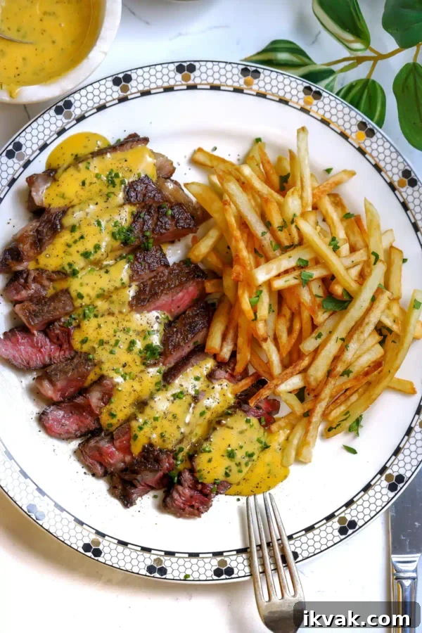 Caesar-Style Whipped Butter: Creamy Dressing-Inspired Spread 4 Top-down view of a round white plate with a black and gold geometric border holding sliced steak with sauce and a mound of french fries.