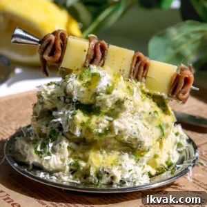 Caesar-Style Whipped Butter: Creamy Dressing-Inspired Spread 9 A close-up of Caesar whipped butter piled on a plate over French-script parchment paper, topped with fresh herbs, grated cheese, and an anchovy and parmesan skewer with a lemon in the background.