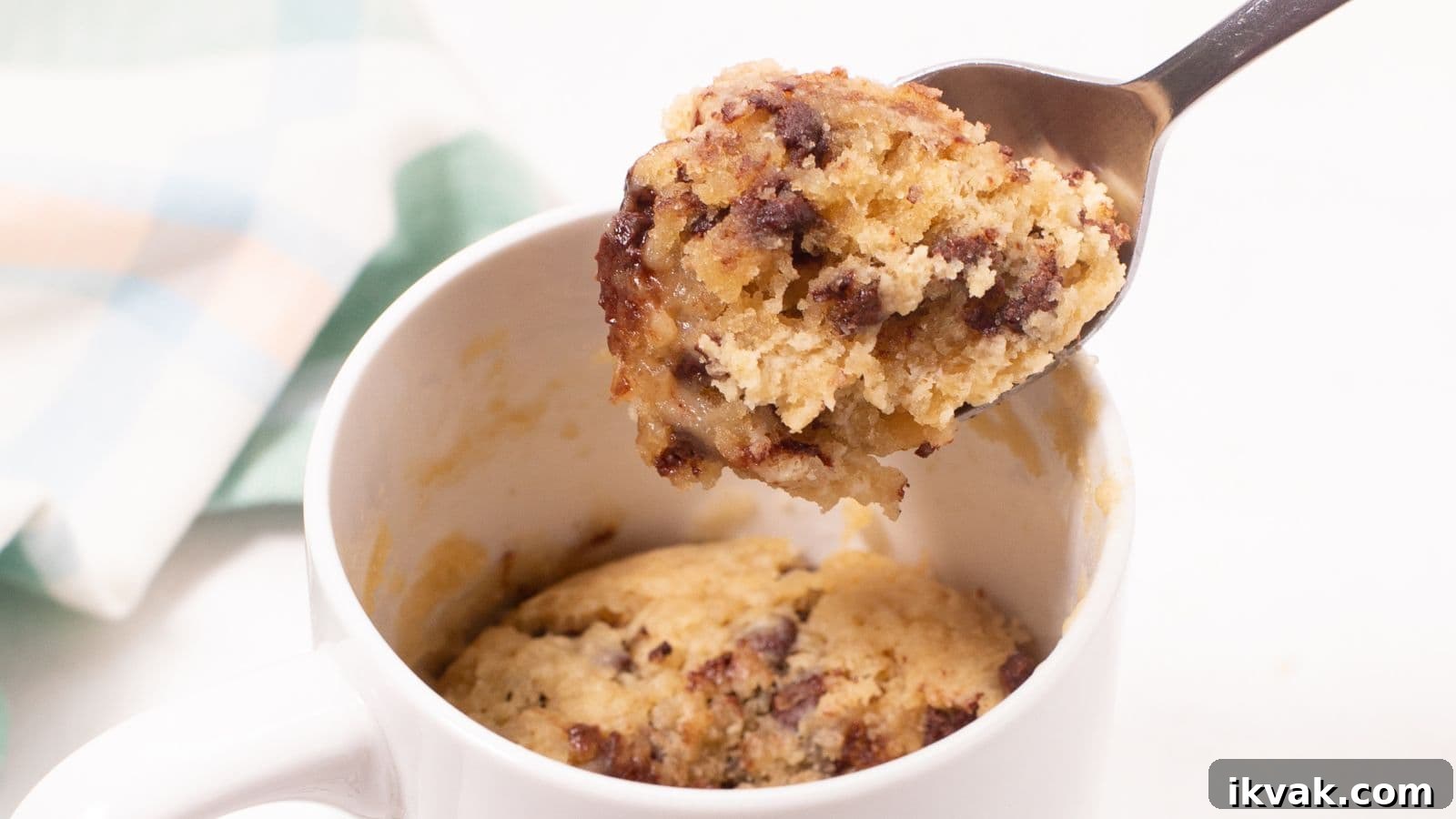 11 Mess-Free Mug Cake Recipes for Quick Single-Serve Desserts 2 A spoon lifting a bite from a chocolate chip mug cake inside a white mug.