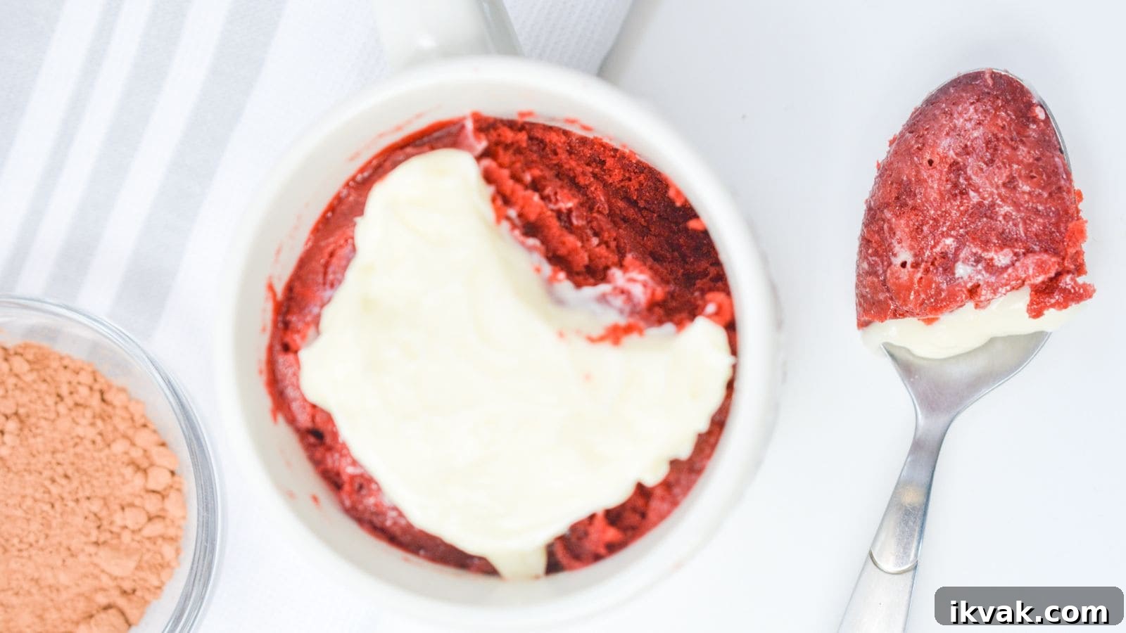 11 Mess-Free Mug Cake Recipes for Quick Single-Serve Desserts 12 Red velvet cake with a layer of cream cheese frosting in a white ramekin, next to a spoon with a bite taken out, on a white background.