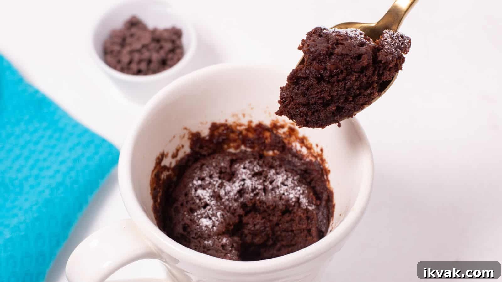 11 Mess-Free Mug Cake Recipes for Quick Single-Serve Desserts 3 A spoon lifting a bite of freshly made chocolate mug cake from a white mug, with chocolate chips in a small bowl in the background.