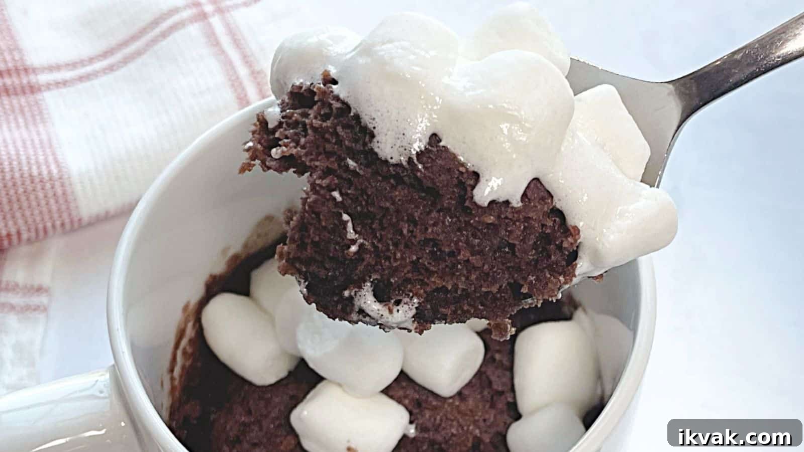 11 Mess-Free Mug Cake Recipes for Quick Single-Serve Desserts 4 A spoon lifting a bite of chocolate mug cake topped with melted marshmallows from a white mug.