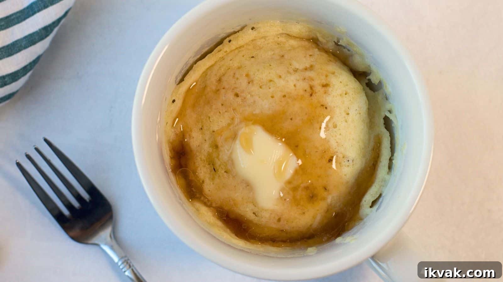 11 Mess-Free Mug Cake Recipes for Quick Single-Serve Desserts 7 A pancake mug cake with syrup on top, viewed from above, next to a fork on a marble surface.