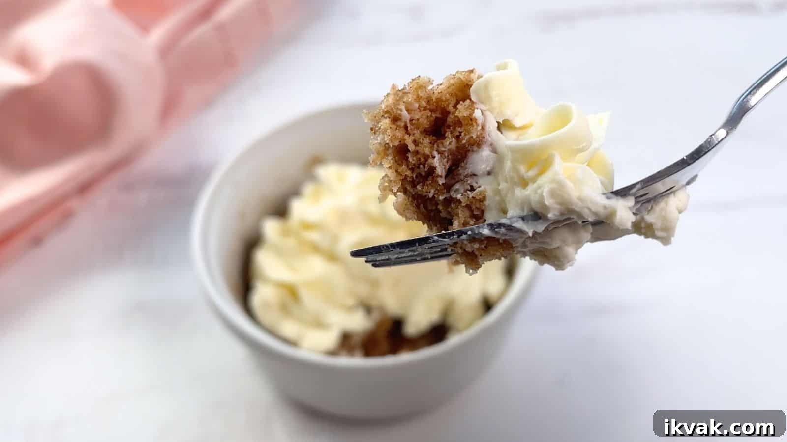 11 Mess-Free Mug Cake Recipes for Quick Single-Serve Desserts 10 A fork holding a piece of cake with cream cheese frosting over a frosted cake mix mug cake on a table.