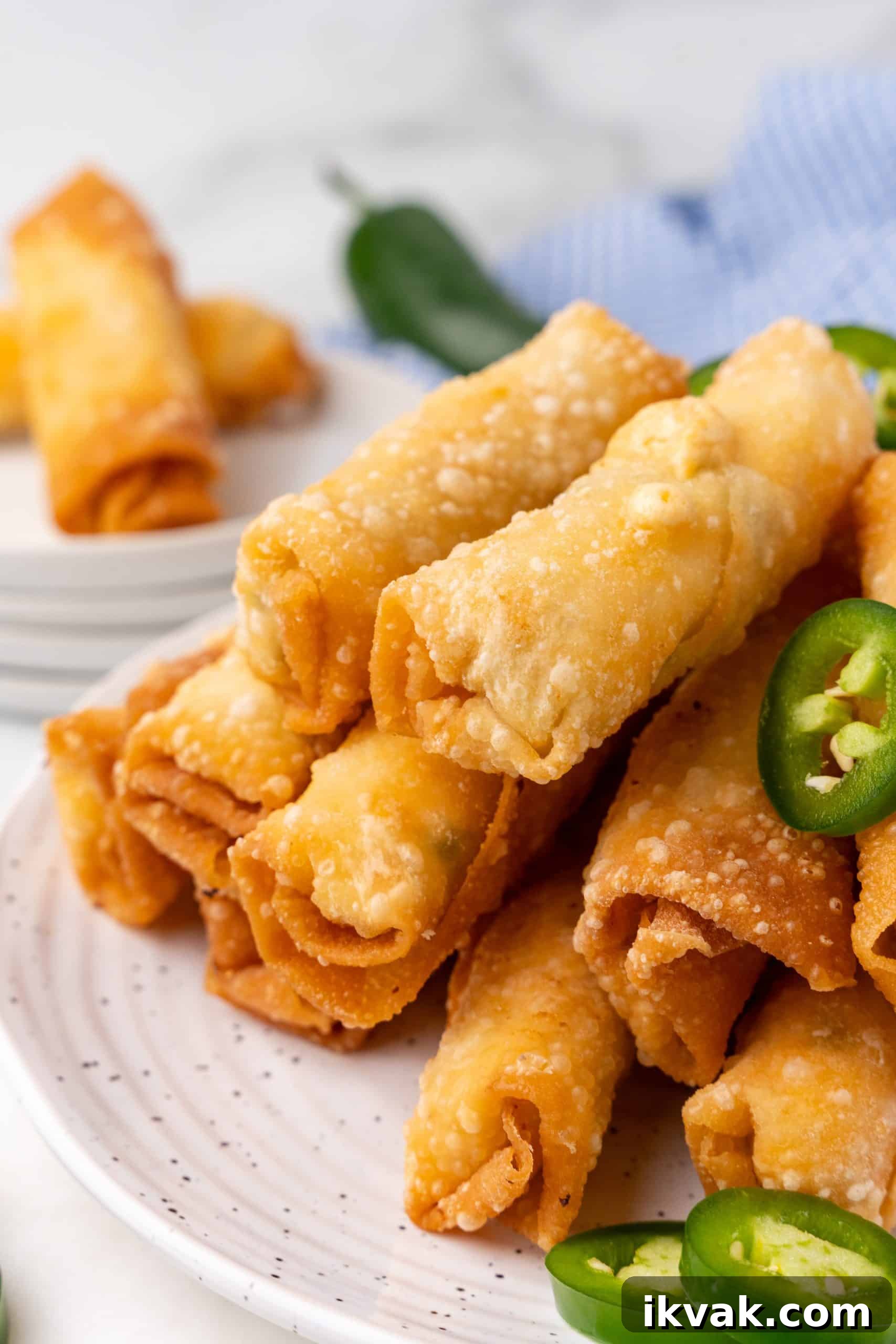 Jalapeño Popper Egg Rolls Recipe — Crispy Stuffed Jalapeño Rolls 3 jalapeno popper egg rolls stacked on small white plates