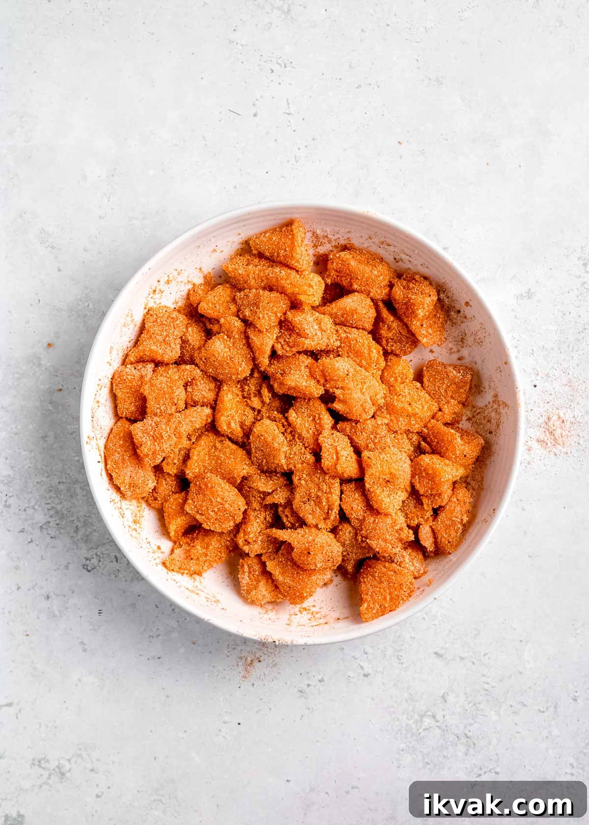 Crispy Air Fryer Buffalo Chicken Bites with Blue Cheese Dip 5 raw chicken being seasoned and sauce added in white bowl