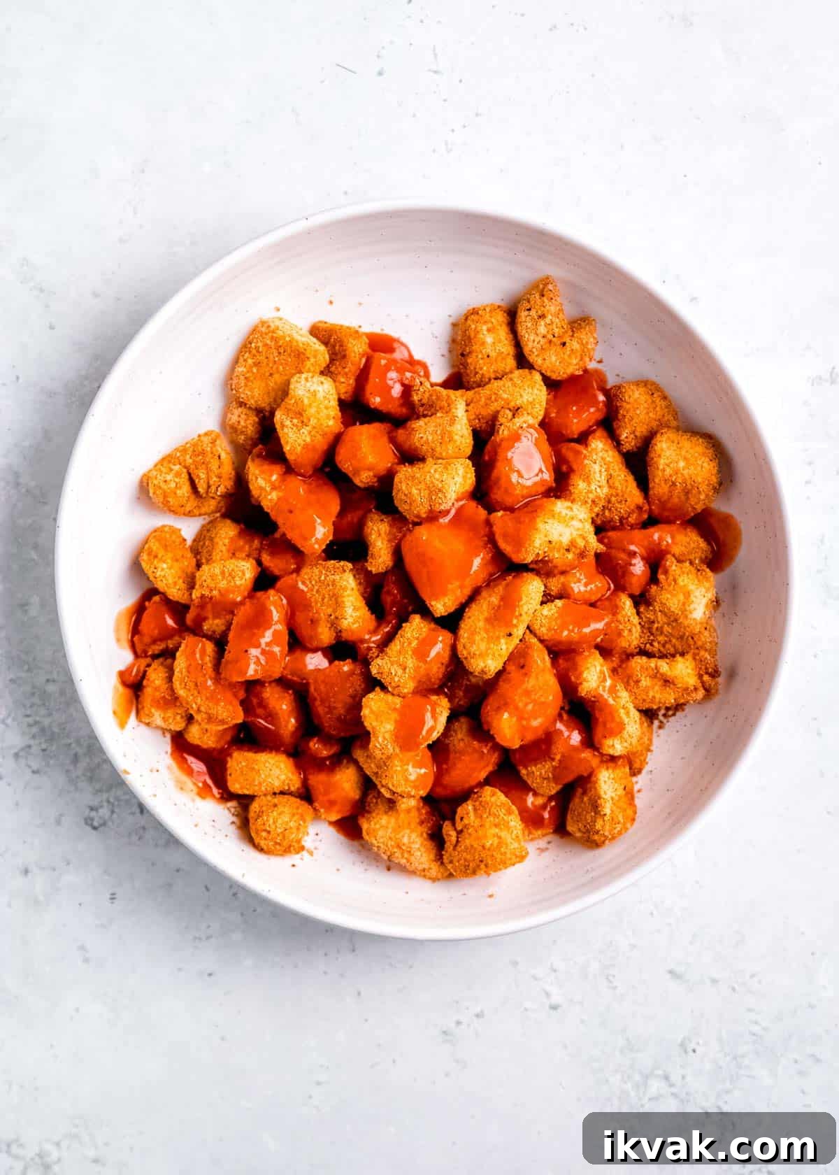 Crispy Air Fryer Buffalo Chicken Bites with Blue Cheese Dip 7 buffalo sauce being added to chicken bites