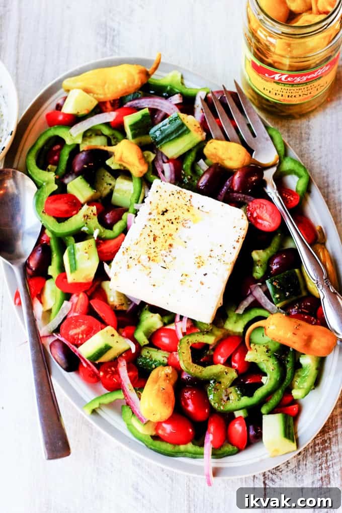 Horiatiki Salad on a plate with jar of peppers on a side