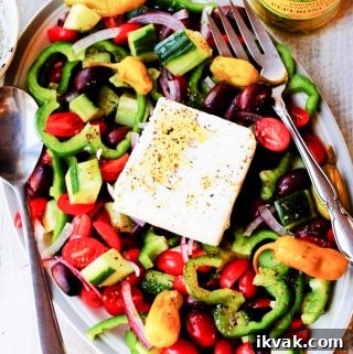 Horiatiki Greek Salad on a plate with jar of peppers on a side