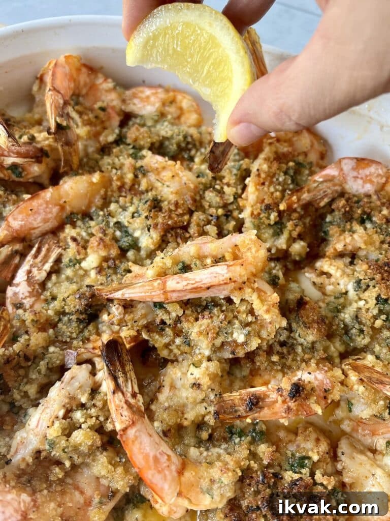 Shrimp Oreganata with White Wine Lemon Butter 9 Lemon wedge being squeezed over pan of finished baked shrimp.