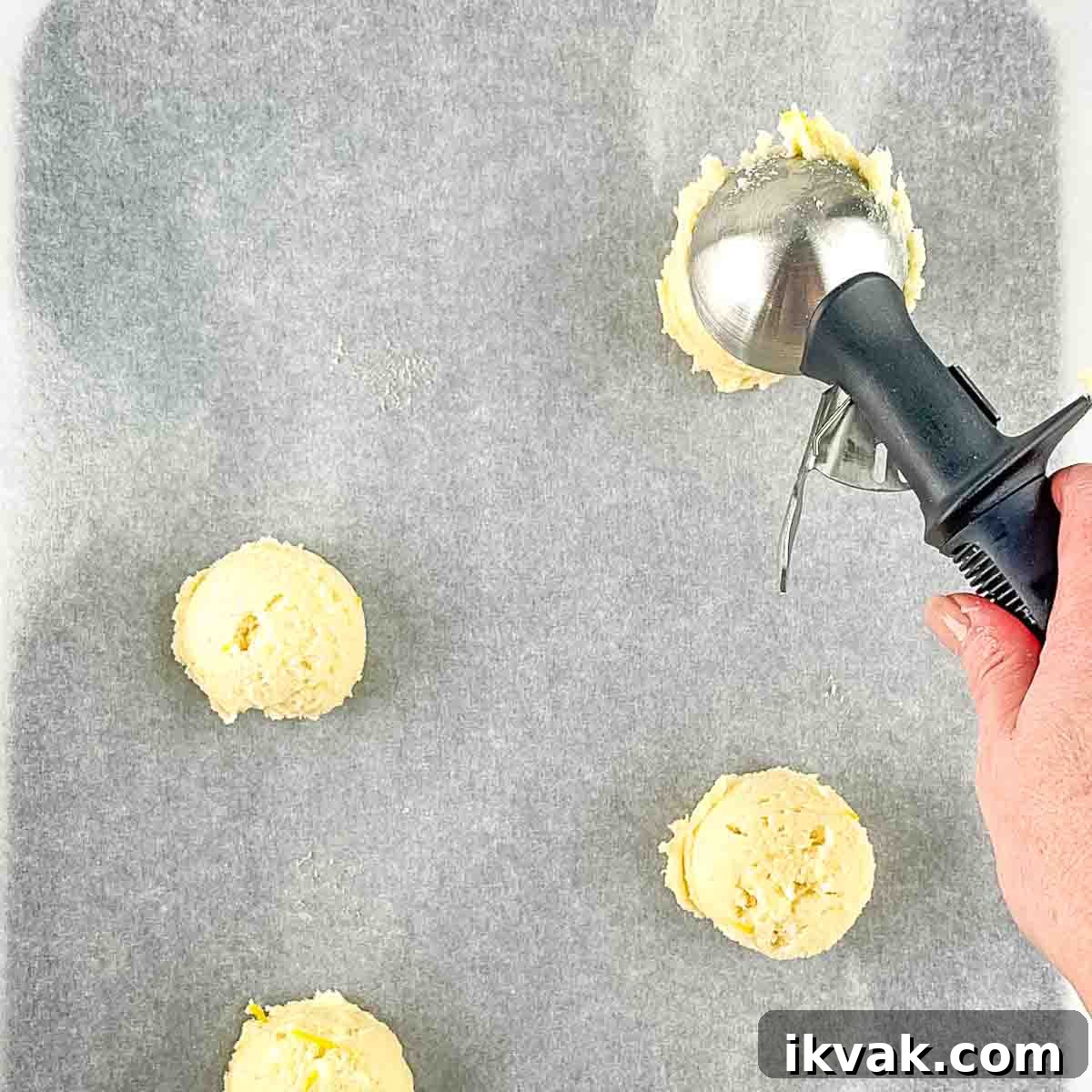 Lemon Drop Cookies Recipe: Soft, Chewy Cookies Like Panera 8 A hand using an ice cream scoop to drop the cookie dough onto a parchment paper lined cookie sheet.