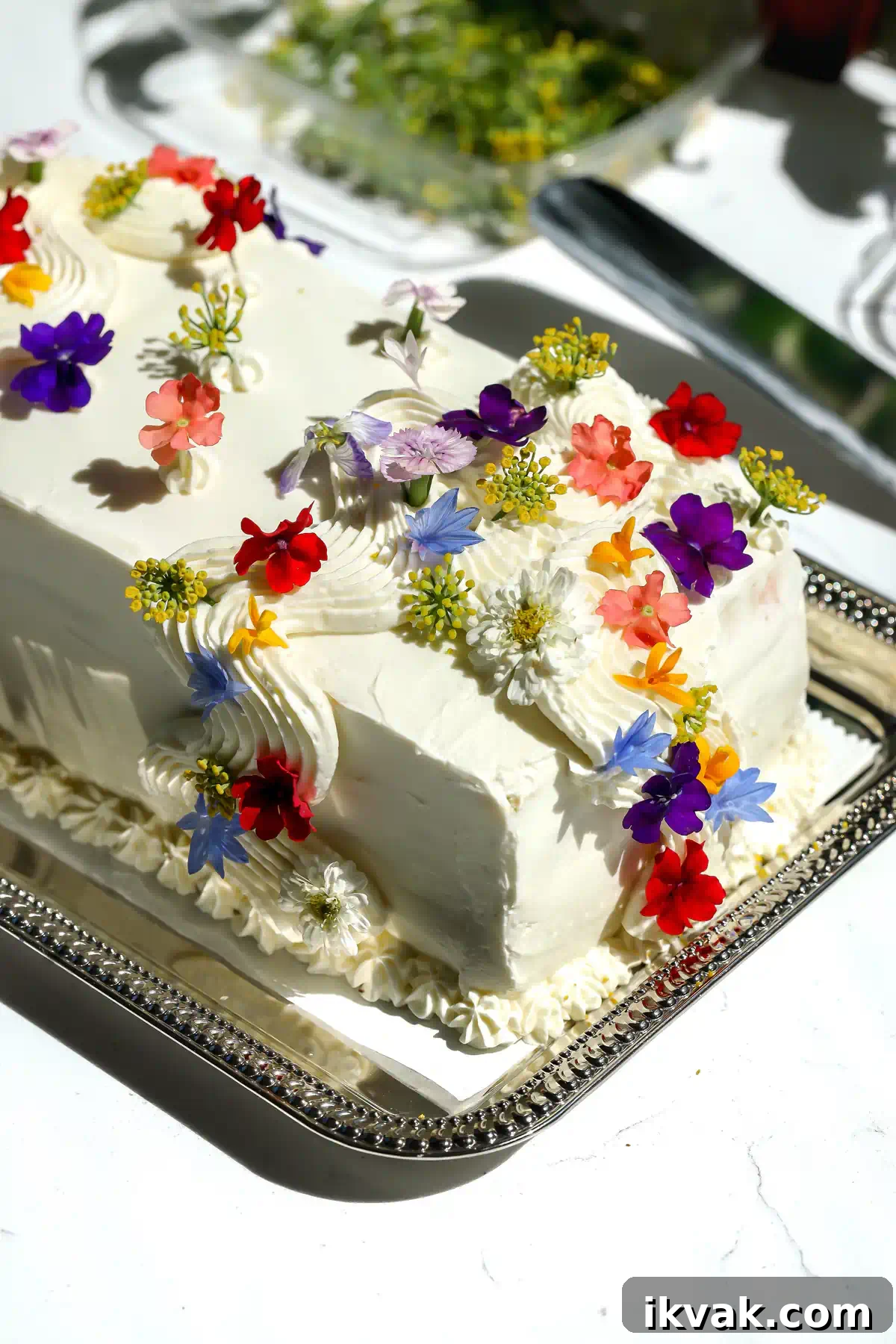 Sandwichon: Classic Homemade Sandwich Recipe 3 Mexican sandwich cake with white cream cheese frosting topped with red, purple, blue, and orange edible flowers on a silver tray.
