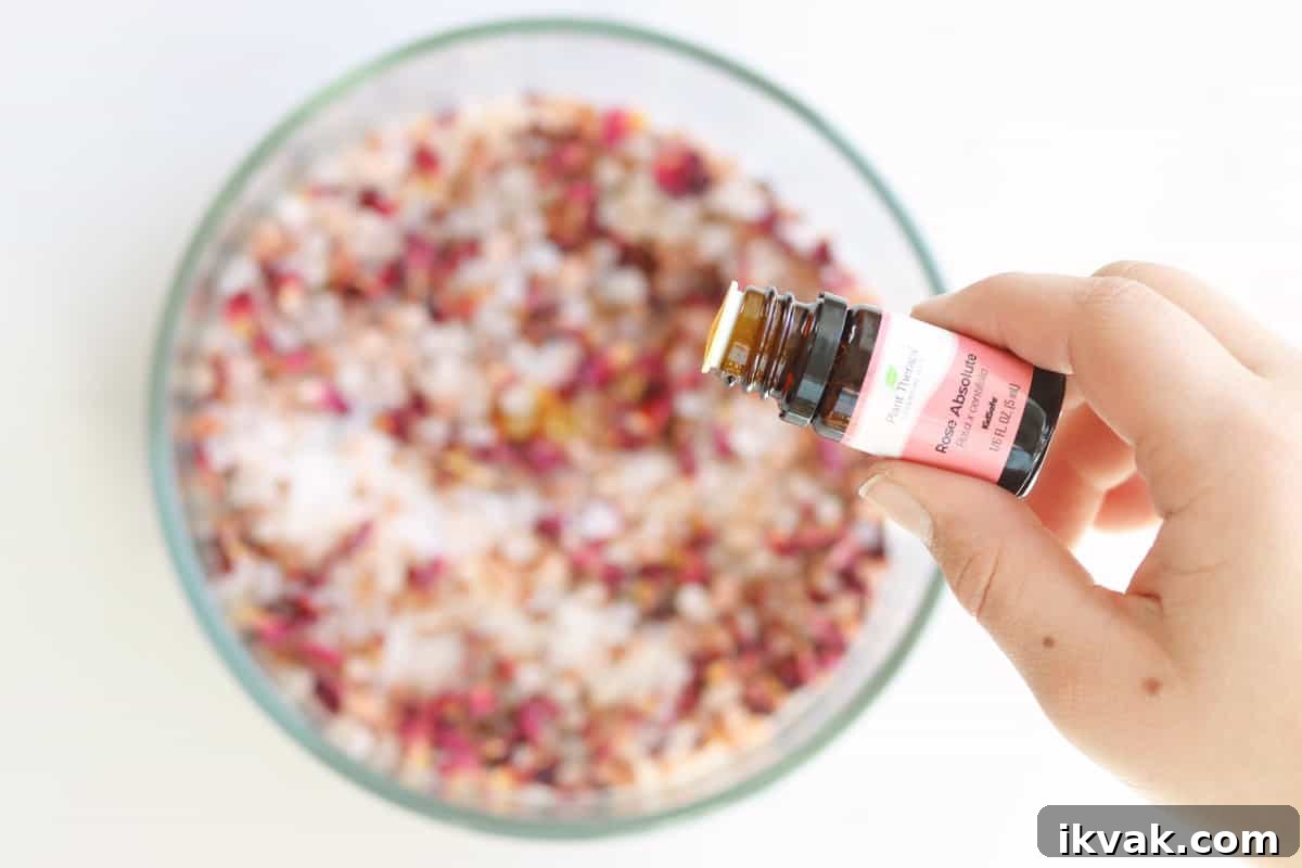 drops of rose essential oil being added to a bowl of sea salt, Himalayan pink salt and rose petals to make bath salts