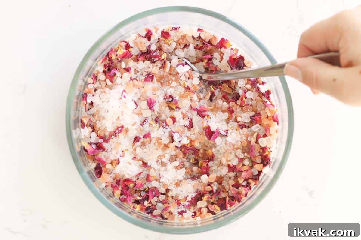 a bowl of sea salt, Himalayan pink salt and rose petals being stirred with a spoon.