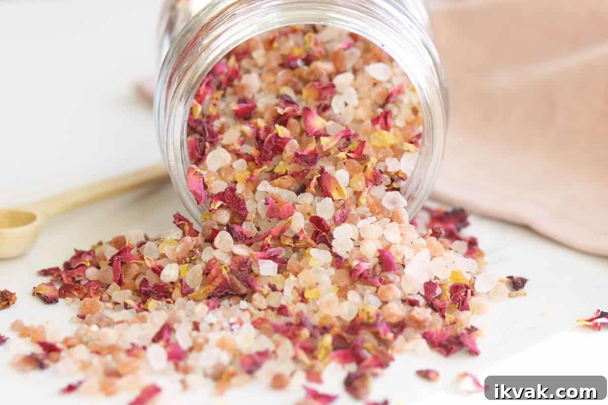 a small glass jar with a wooden lid and small wooden spoon full of rose bath salts with rose petals in it.