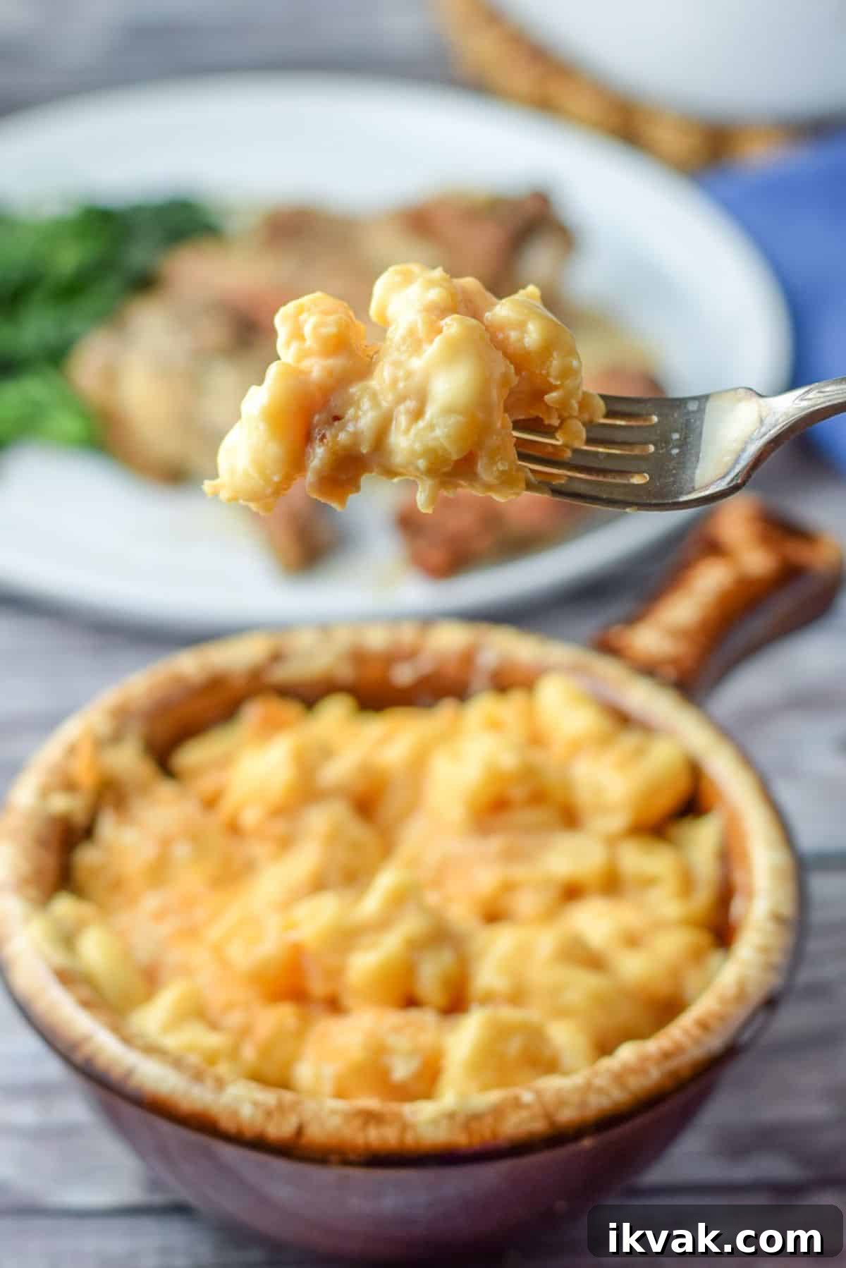 Ultimate Creamy Baked Mac and Cheese Recipe 8 A forkful of cheesy macaroni over a crock filled with it - also with a plate in the background