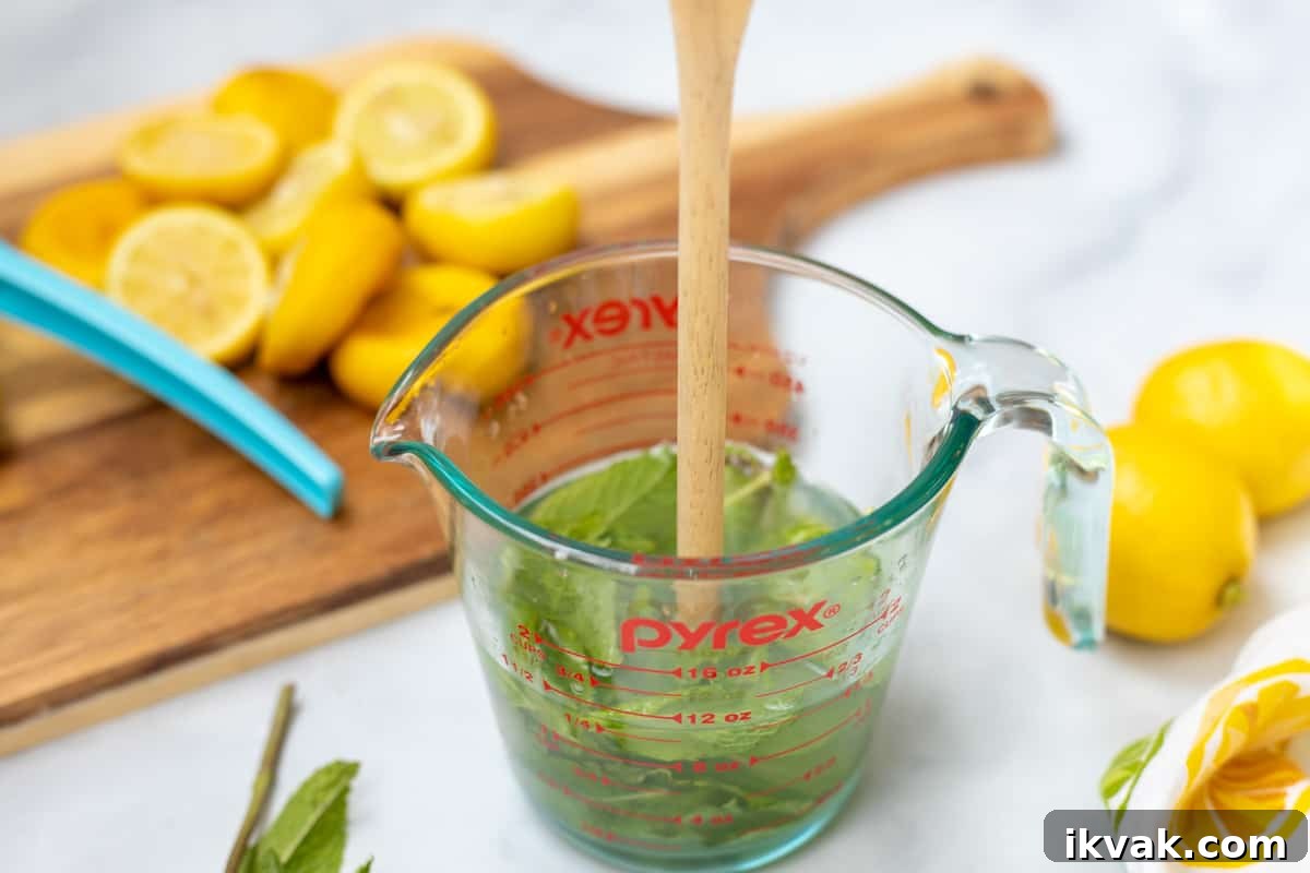 Mint leaves being muddled with a wooden spoon in a glass measuring cup.