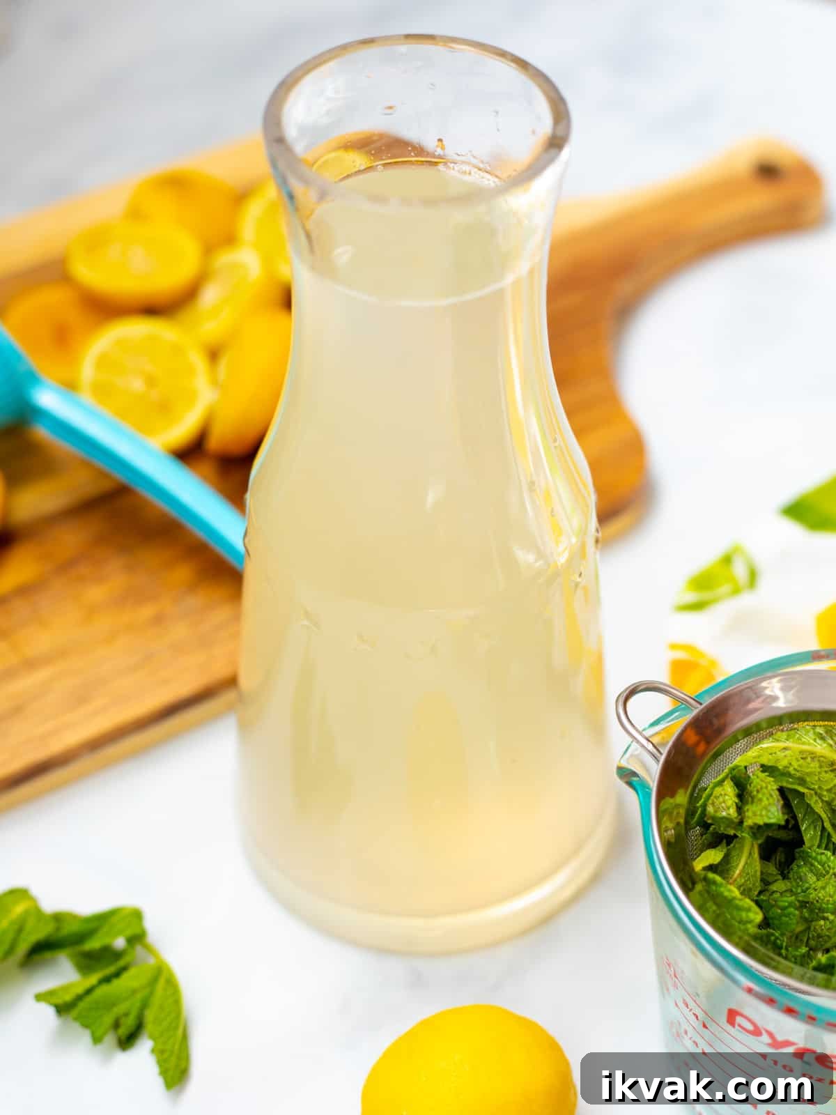Clear pitcher of mint lemonade next to fresh mint and lemons.