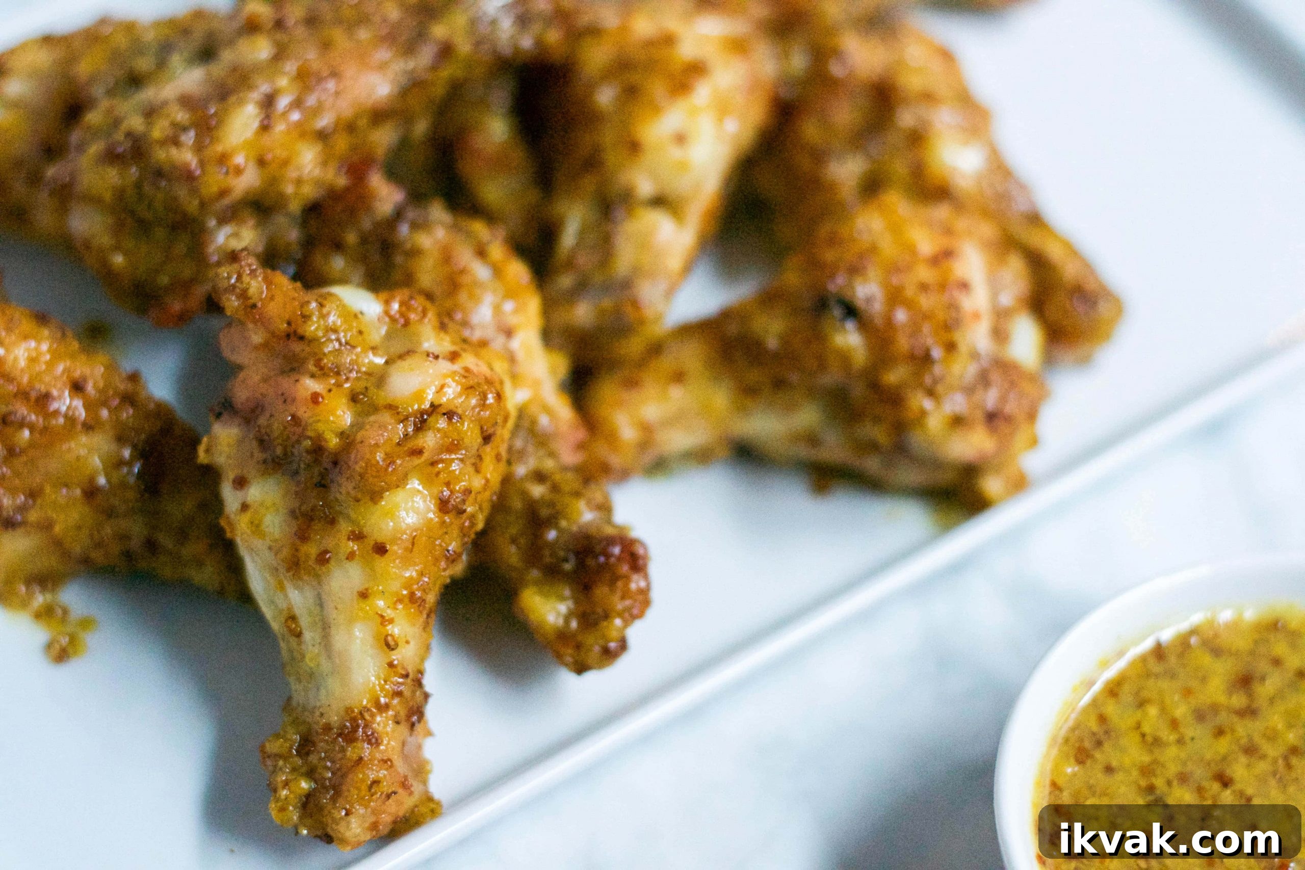 Crispy Honey Mustard Baked Chicken Wings Recipe 5 Close-up of Honey Mustard Baked Chicken Wings on a white plate, served alongside a small bowl of grainy mustard dipping sauce.