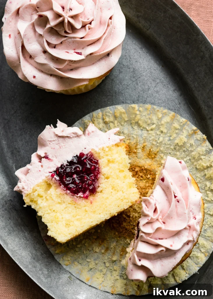 Sliced lemon cupcake with raspberry jam filling and raspberry icing laying cut side open on a plate.