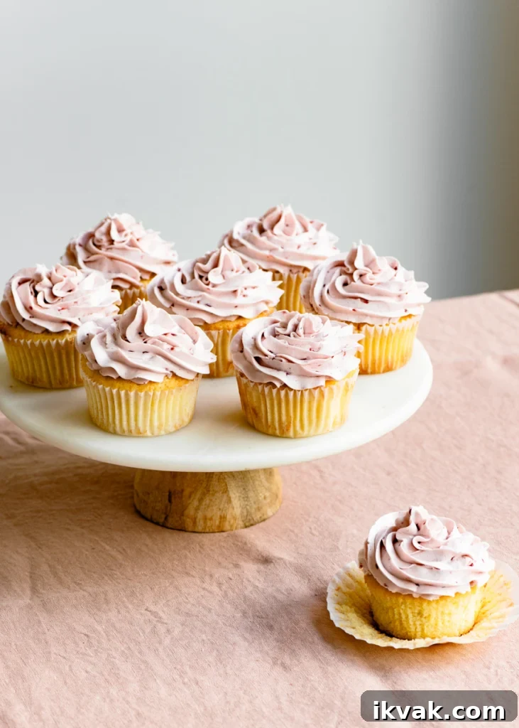 Cake stand full of raspberry frosting topped lemon cupcakes on a linen covered table.