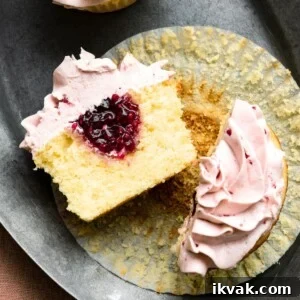 Sliced lemon cupcake with raspberry jam filling and raspberry icing laying cut side open on a plate.