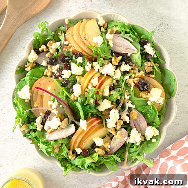 Top view of shallow bowl with apple walnut green salad with feta and cranberries. White surface.