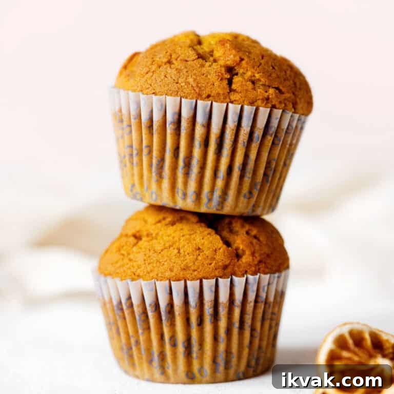 Close up image of two stacked pumpkin muffins on a white surface with pink background.