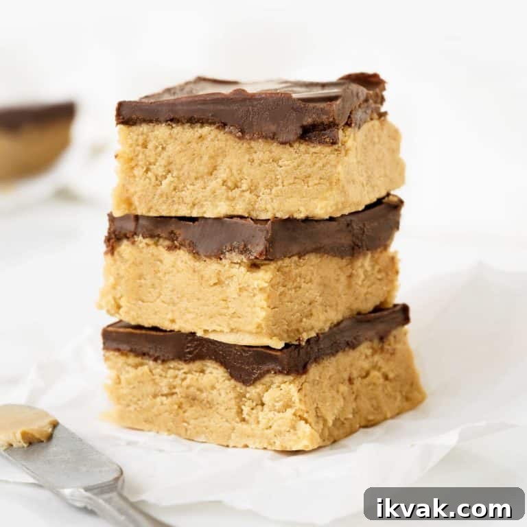 Three squares of peanut butter chocolate fudge on a white paper and white surface.