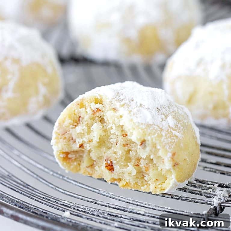Bitten snowball cookie on a wire rack with whole ones in the background.