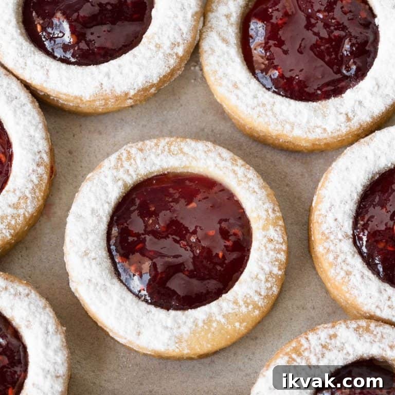 Close up of raspberry linzer cookies on a beige surface.