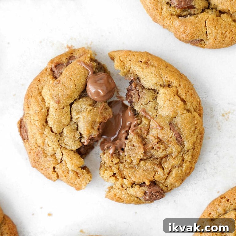 Close up of halved warm milk chocolate chip cookie on white parchment paper.